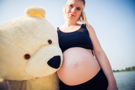 Portrait of a young and beautiful pregnant woman with a big teddy bear.の写真素材