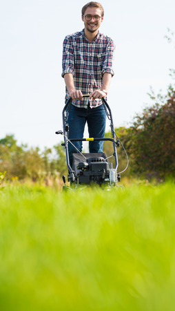 Photo of a young man mowing the grass during a sunny day.