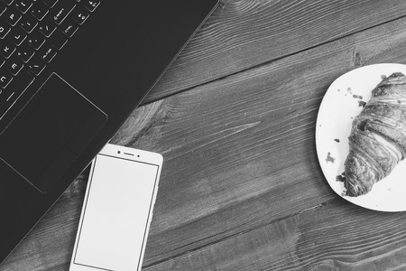 Workspace with laptop, smartphone and croissant on wooden deskの写真素材