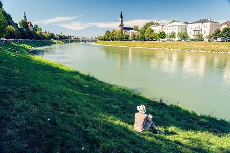 Man sitting on the Salzach river bank in Salzburg, well known city in Austria, since 1996 listed as a UNESCO World Heritage Site.の写真素材