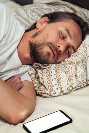 Phone in bed next to a handsome young man that is taking a nap. Phone's screen is turned on.の写真素材