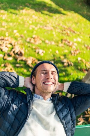 Happy young man on a bench during a sunny autumn day.の写真素材