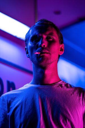 Vintage, red and blue portrait of a young man smoking a cigarette. Street lights visible in the...