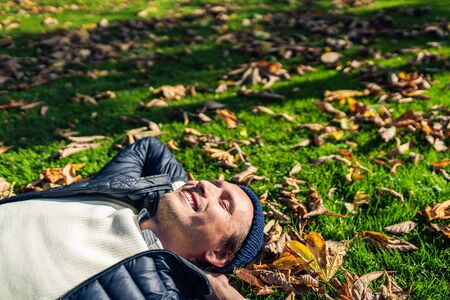 Happy young man relaxing in the park among autumn leaves.の写真素材