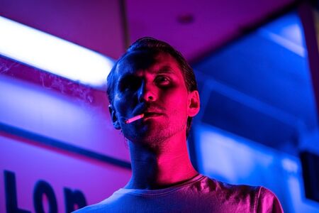 Vintage, red and blue portrait of a young man smoking a cigarette. Street lights visible in the background.の写真素材