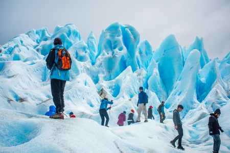 Tourists stand on the slopes of the glacier. Blue glacier in the sunlight. Uneven surface of the glacier in the sun. Beautiful blue glacier against the sky.のeditorial素材