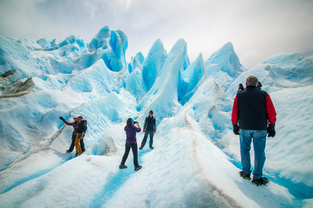 Tourists photograph each other on the slopes of the glacier. Blue glacier in the sunlight. Uneven surface of the glacier in the sun. Beautiful blue glacier against the sky.のeditorial素材