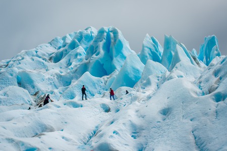 Tourists stand on a glacier in the distance. Blue glacier in the sunlight. Uneven surface of the glacier in the sun. Beautiful blue glacier against the sky.のeditorial素材
