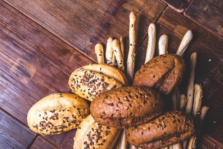 Top view of a bunch of baking on a wooden table. Top view of a crispy pastry strewn with seeds. Buns and bread sticks lie on a wooden table. Buns of wheat and rye flour lie on bread sticks.の写真素材