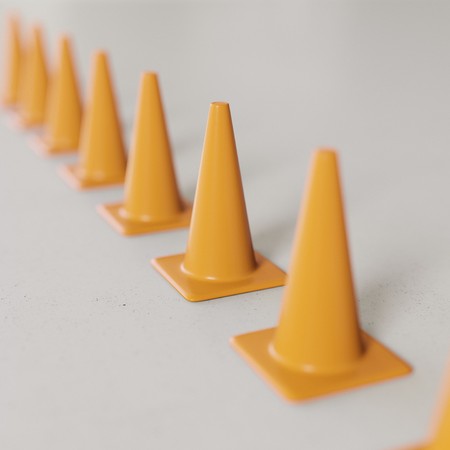 Perfect line of simple orange traffic cones on a seamless concrete floor. This image features a shallow depth of field and is a 3d render.の写真素材