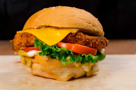 Close Up On Crispy Chicken Burger With Cheese Lettuce and Tomato. Tasty Chicken Burger on Dark Background.の写真素材