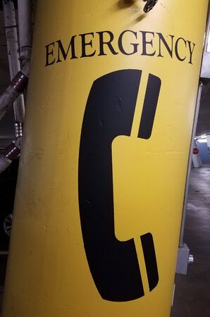 black emergency telephone symbol on a yellow cement pillarの写真素材
