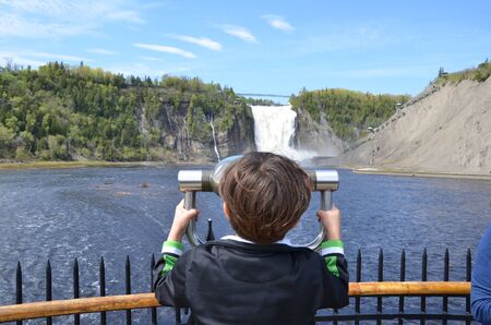 boy child looking through viewfinder or binoculars at a waterfall in Quebec, Canadaの写真素材