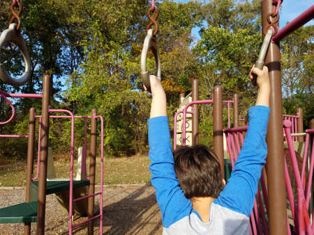 boy child hanging from metal rings on playground