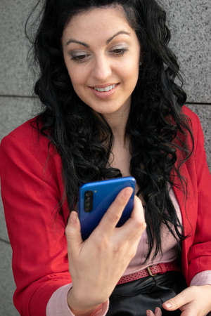 young woman having fun with mobile with red jacket and blue mobile