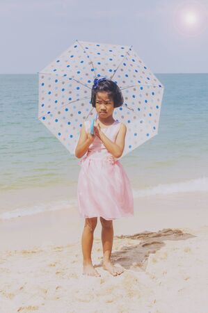 Umbrella little girl stand on the sand and blue skyの写真素材
