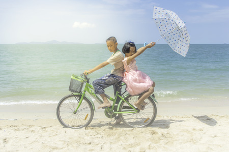 Happy little girl and boy ride bicycle playing on the beach.の写真素材