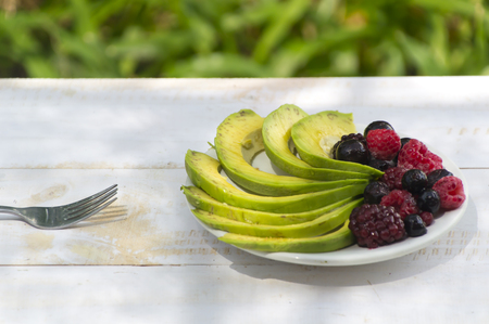 Healthy breakfast ingredients avocado slices with mix berries and honey.