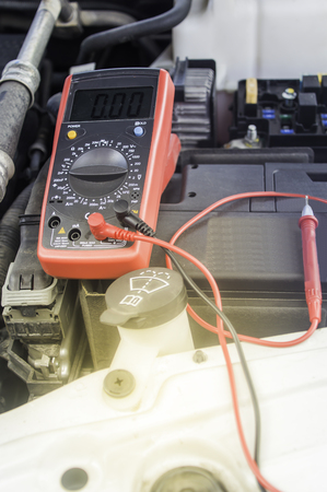 Auto mechanic uses a multimeter voltmeter to check the voltage level in a car battery,Selective...