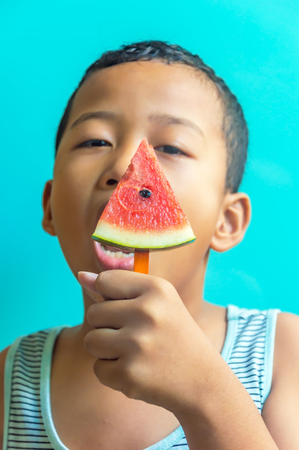 Happy asian boy summer watermelon slice popsicles on a blue rustic wood background. copy space for designerのeditorial素材
