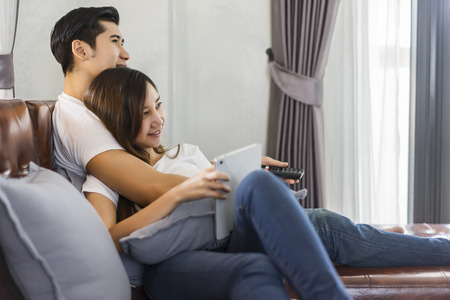 Young couple in love sitting on a brown sofa and watching television in the living room.の写真素材