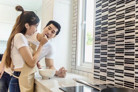 Sweet couple home kitchen cooking lover concept.Young asian woman holding salad to man eating each for cooking dinner healthy food menu in kitchen romantic.の写真素材