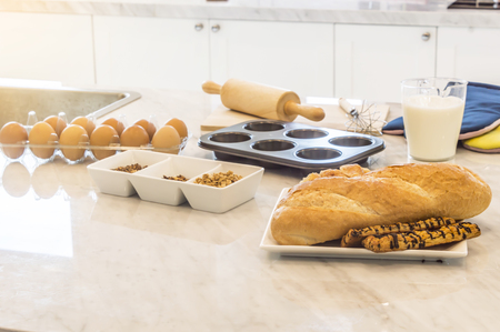 Freshly baked baguette and bread with ingredients for whole grain healthy bread,Granola and milk and eggs in the kitchen.の写真素材