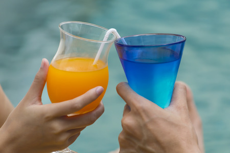 Happy couple with two glasses of orange juice at swiming pool.の写真素材