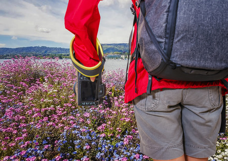 Hiker woman traveler with photo camera and backpack on the flowers garden, admiring mountain lake...