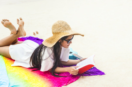 Summer woman relaxing in hipster beach hat and colorful sunglasses. Funky happy girl having fun during travel holidays vacation. Young trendy cool hipster woman reading a book and lying in the sand.の写真素材
