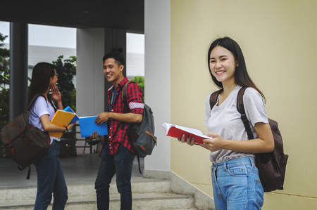 Young Asian woman student and friends are tutoring exam with study book and laptop in back side, Student group and tutoring education concept.の写真素材