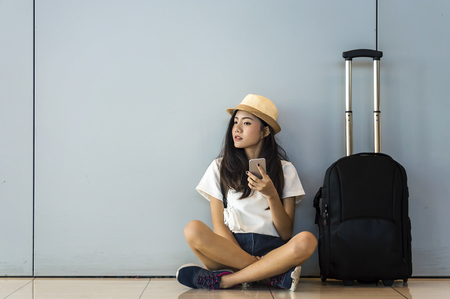 Airport Young female passenger on smart phone  sitting in terminal hall waiting for her flightの写真素材
