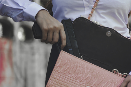 Office woman hiding gun safety self from robber thief mask danger for stop gangster on street.の写真素材