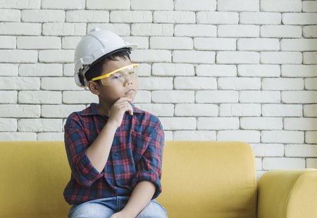 Little boy wearing a engineering helmet and looking throught window. Arms crossed on chest.の写真素材