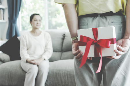 Happy senior couple Man surprising his girlfriend with a gift on the couch at home in the living room - Imageの写真素材