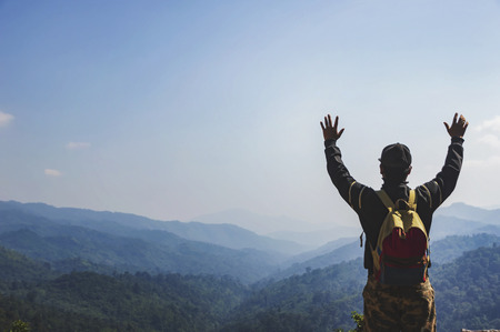 Young man hiker with backpack standing on top of a mountain with raised hands.の写真素材
