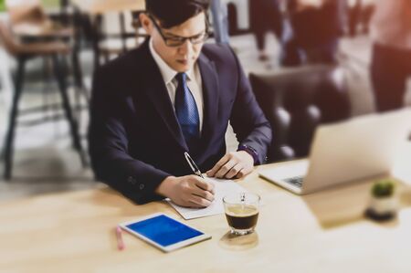 Confident businessman in eyeglasses looking at the paper and working at table with computer monitor in modern office.の写真素材