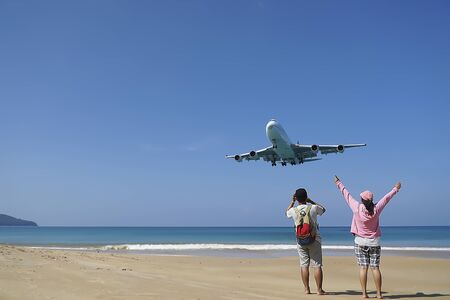 Couples have fun on the beach watching the landing planes. Traveling on an airplane concept. Amazing landscape.の写真素材