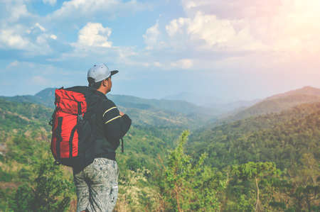 Young asian man tourist with backpack relaxing on top rock and enjoying sunset. Lifestyle Travel happy emotions success concept summer vacations outdoor. Hiker tramping up famous trail.の写真素材