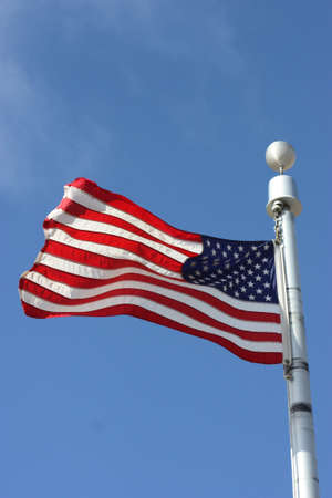 A US FLAG on a flag pole blowing in the wind with bluesky.