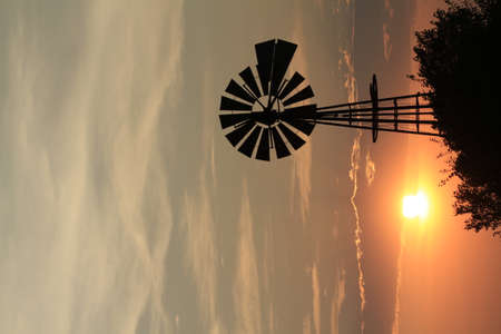 A shot of a Kansas Windmill at Sunset with clouds and the Sun with a colorful Sky out in the country north of Hutchinson Kansas USA.の写真素材