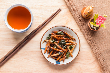Fried insects - Wood worm insect crispy with pandan after fried and add a light coating of sauce and garnish Thai pepper powder with chopsticks, tea, brown cloth on wooden background, Top viewの写真素材