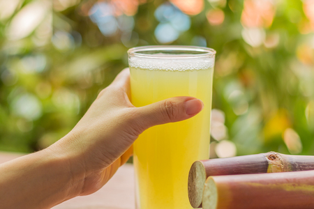 Sugarcane fresh juice for healthy eating. Close up of woman hands with sugarcane fresh juice on wooden background.の写真素材