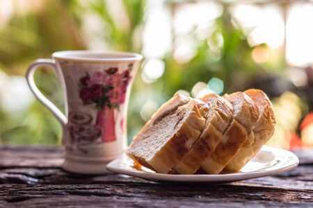 Sliced bread - Homemade slices of bread on a white plate and cup of coffee on old wooden table background. Select focus.の写真素材