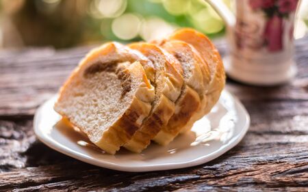 Sliced bread - Homemade slices of bread on a white plate and cup of coffee on old wooden table background. Select focus.の写真素材