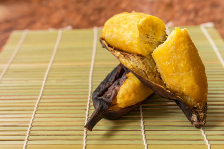 Grilled banana - Delicious golden brown grilled banana in a bamboo mat on wooden table background. Thai dessert. Traditional,  Closeup, Select focusの写真素材