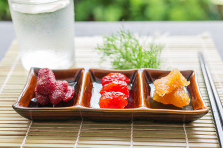 Dried fruit, Dried strawberries, dried tomatoes, pineapple preserves in a small ceramic bowl with chopsticks and Ice water on bamboo place mat. Close up, Selective focusの写真素材