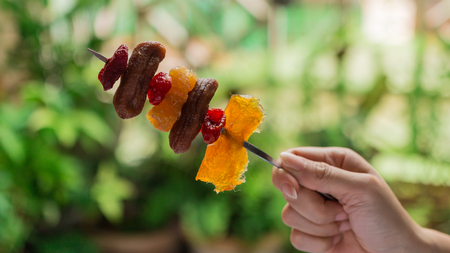 Woman holding stainless steel skewers with dried fruits mixed, horizontal, close-up, select focusの写真素材