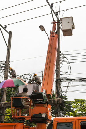 Editorial image of Bangkok, Thailand - August 5, 2017: Electricians at an altitude installs new cable high voltage against the cloudy sky. のeditorial素材