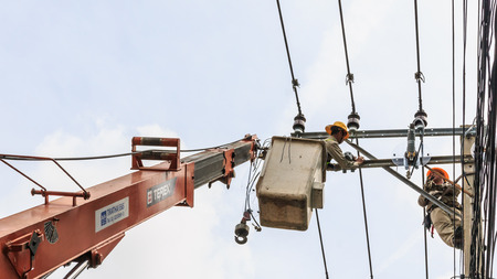 Bangkok, Thailand - August 5, 2017: Electrician working on electric pole at an altitude to installs cable high voltage against with cloudy sky. のeditorial素材